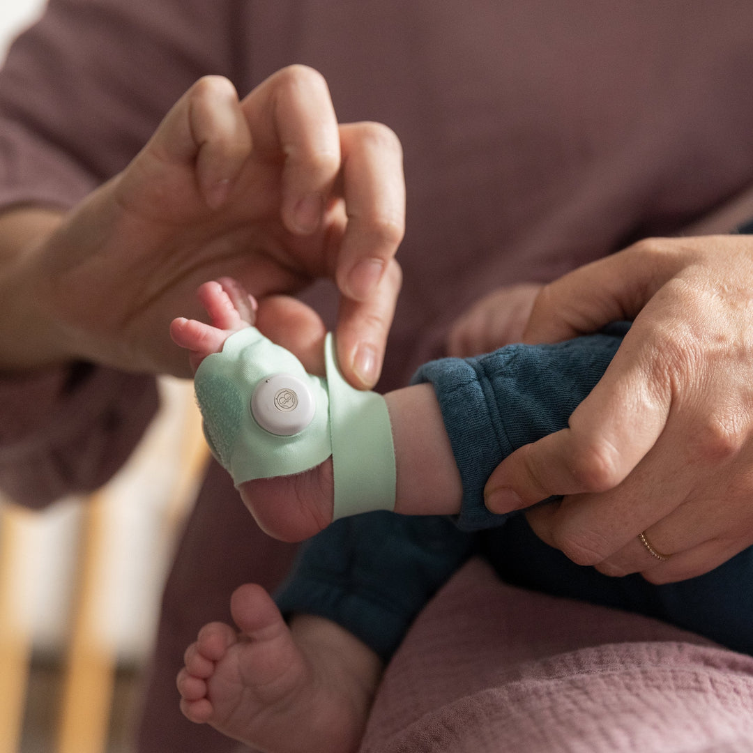 Putting the Owlet Smart Sock 3 mint sensor sock on an infant foot
