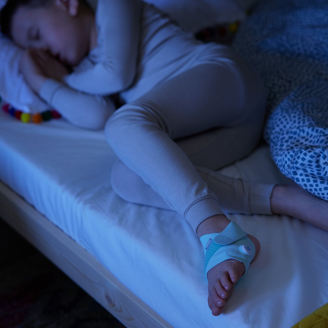 Child sleeping with the Owlet Smart Sock 3 mint sock at night