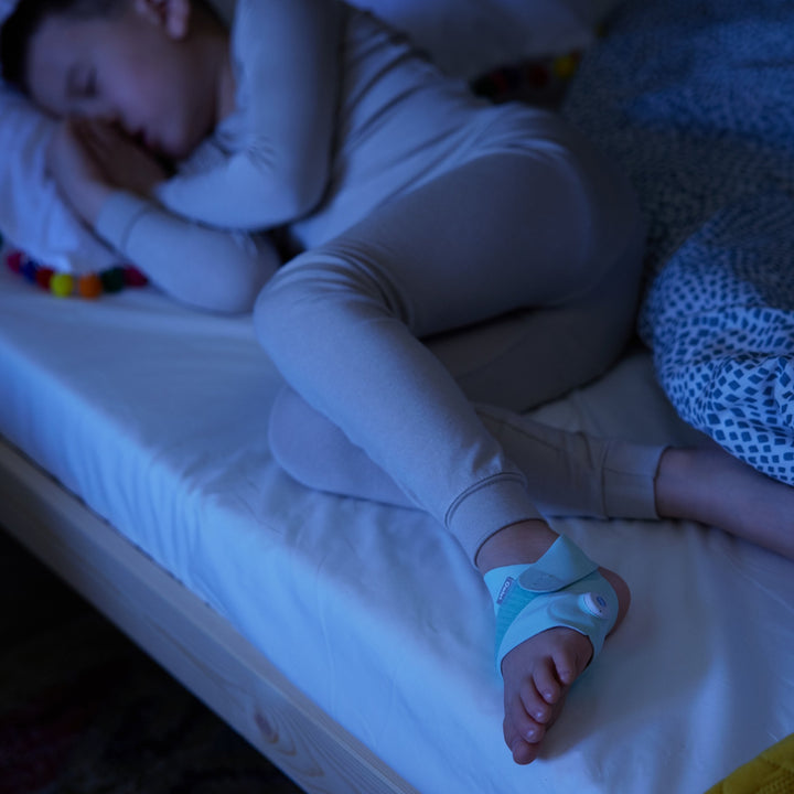 Child sleeping with the Owlet Smart Sock 3 mint sock at night