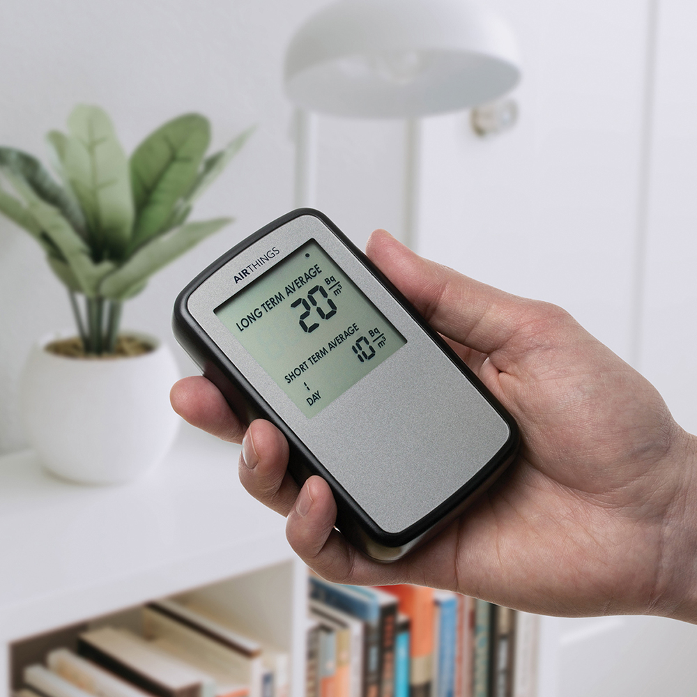 Hand holding the Airthings Corentium Home radon detector indoors, screen reading in Bq/m³