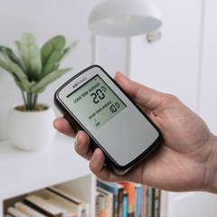 Hand holding the Airthings Corentium Home radon detector indoors, screen reading in Bq/m³