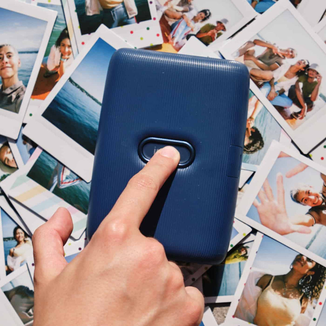A finger pressing the instax button on the Fujifilm INSTAX Mini Link in Dark Denim