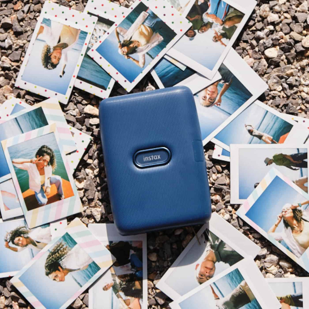 Fujifilm INSTAX Mini Link in Dark Denim lying on a spread of INSTAX Mini prints