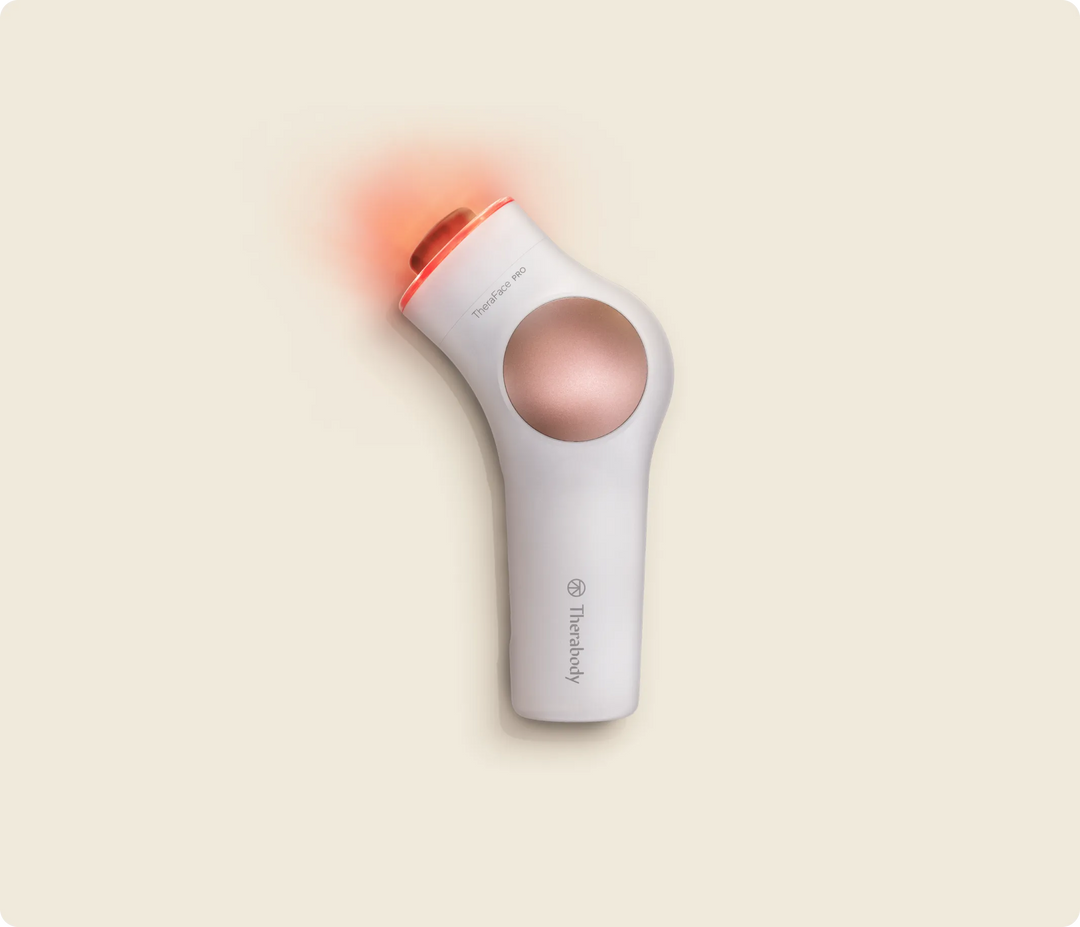 Therabody TheraFace PRO in white with rose gold accent and the LED Light Therapy Ring lit red