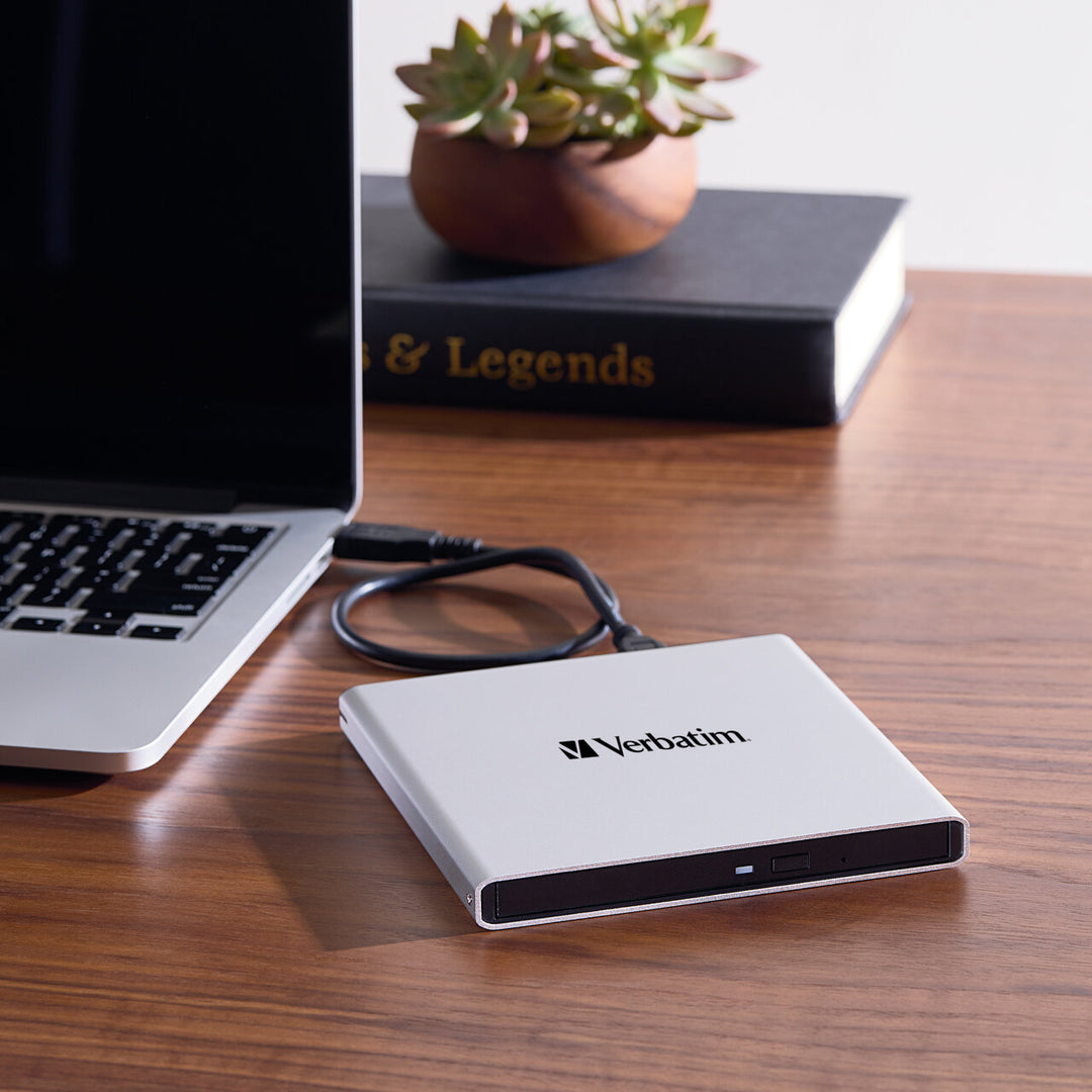 Verbatim External All-in-One Optical Writer connected to a laptop by its USB cable on a wooden desk