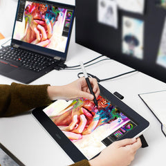 Artist drawing on the Wacom One pen display connected to a laptop on a desk